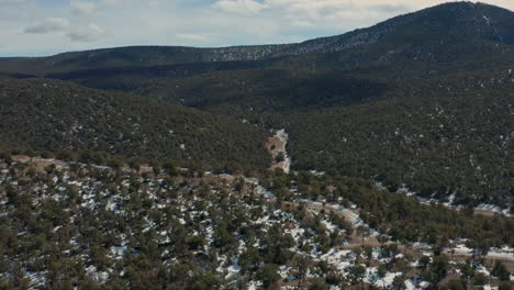 Wide-descending-aerial-of-ATV-driving-down-remote-road-in-desert-mountains