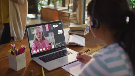 schoolgirl using laptop for online lesson at home, with girl talking and web chat on screen