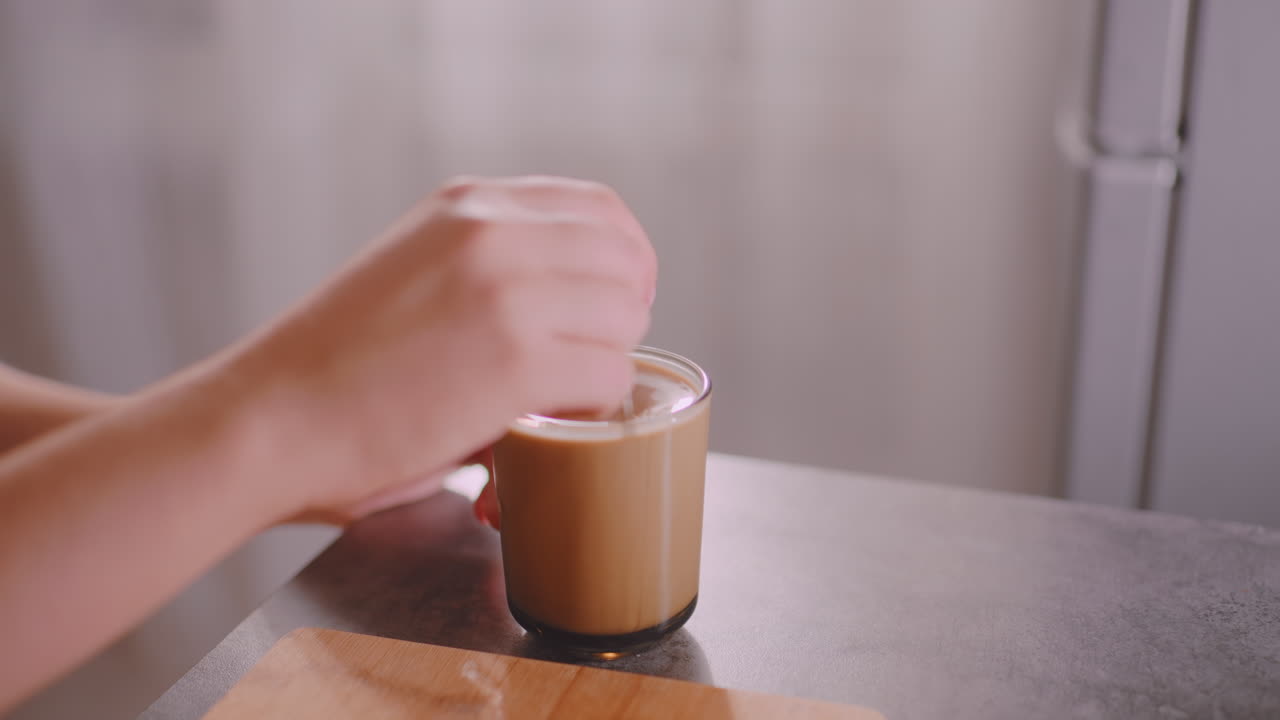 Primo piano di una mano che mescola il tè in una tazza di vetro appoggiata su un tavolo, illuminata da una calda luce interna; il leggero movimento circolare crea delle increspature sulla superficie del liquido