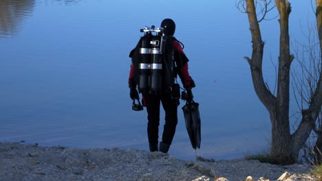 Slow-motion-shot-of-a-professional-scuba-diver-heading-into-a-lake-holding-fins