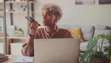 focused ethnic female employee buys with laptop talk on loudspeaker on phone