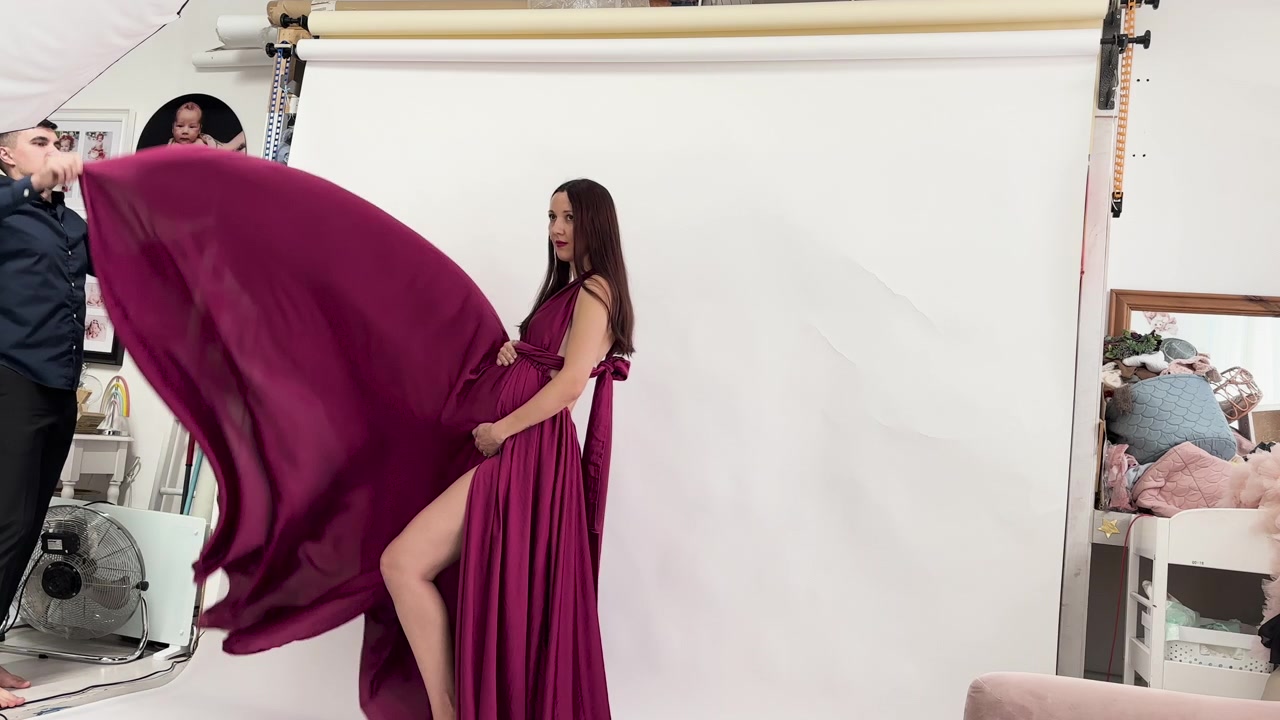 Vista del marito che sventola l'abito color magenta della moglie durante un servizio fotografico di maternità in studio. Donna incinta.
