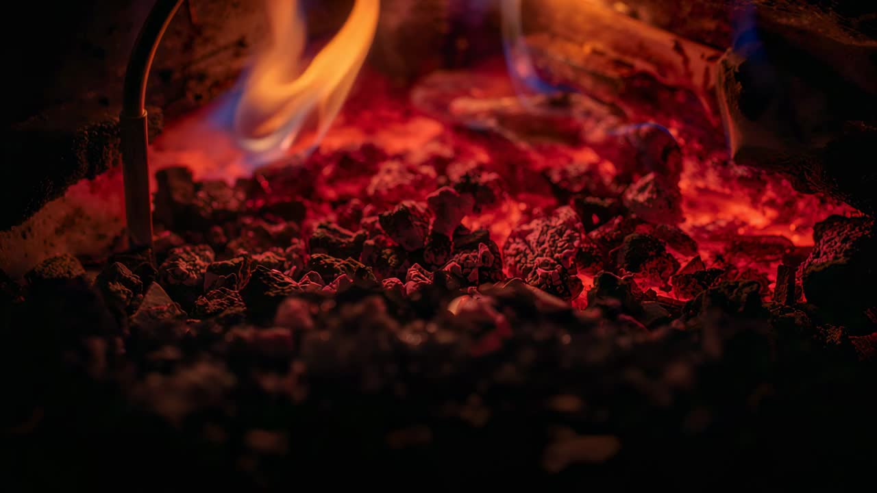 Flickering bed of embers and flame responding to draft, radiating heat inside oven, log visible