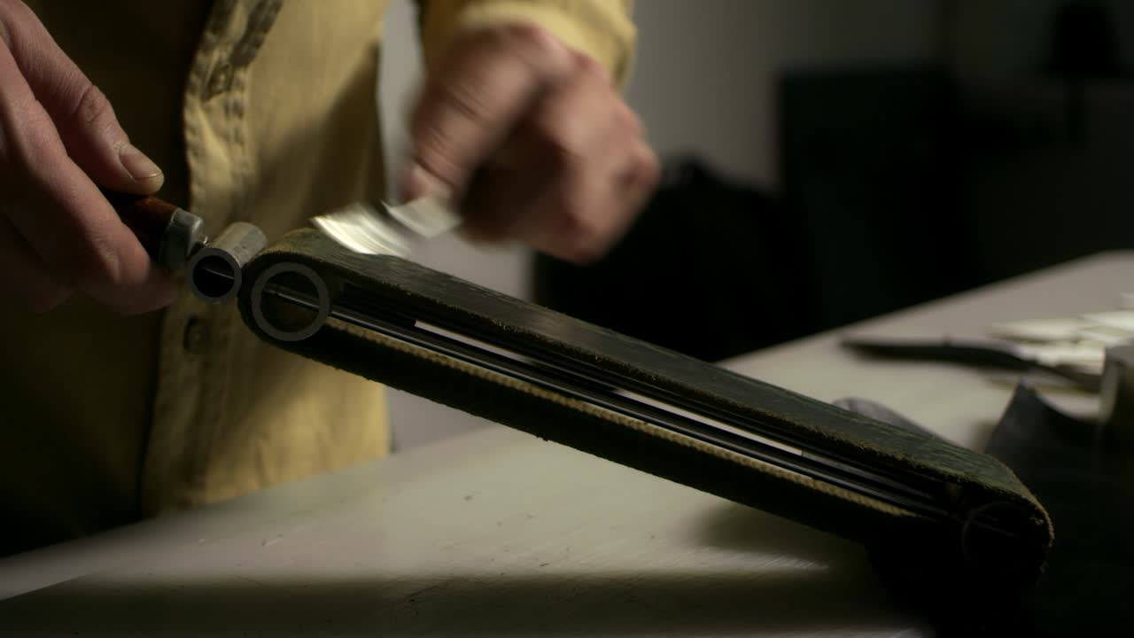 Marroquinero afilando un cuchillo de corte con una piedra de afilar. Primer plano de las manos del hombre.