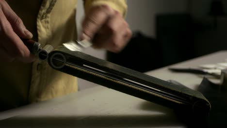 leather maker sharpening stencil knife with whetstone. close up man hands