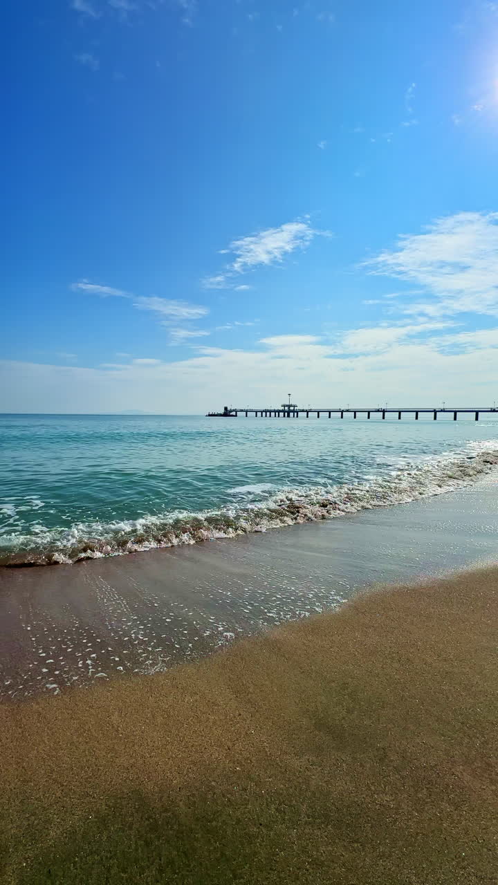 Pemandangan pantai yang damai dengan ombak lembut berdebur di pasir keemasan di bawah langit biru cerah