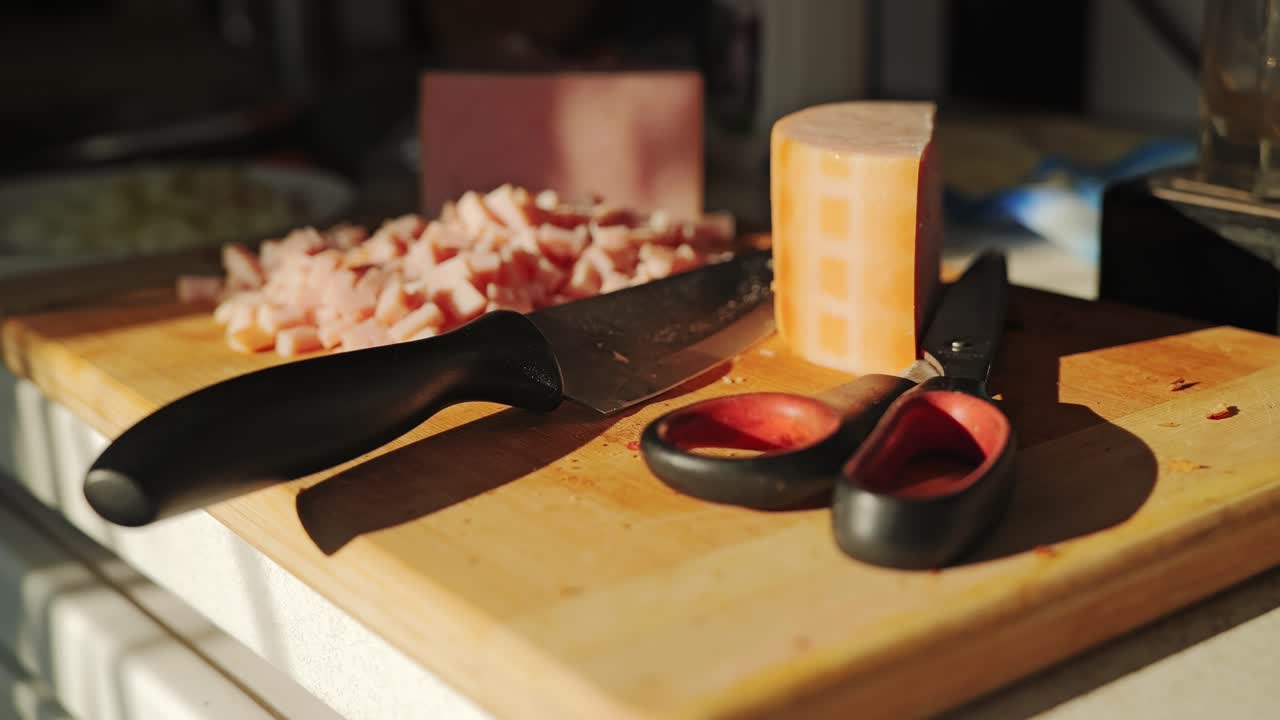 Wooden cutting board with diced ham, kitchen knife and scissors in sunset glow