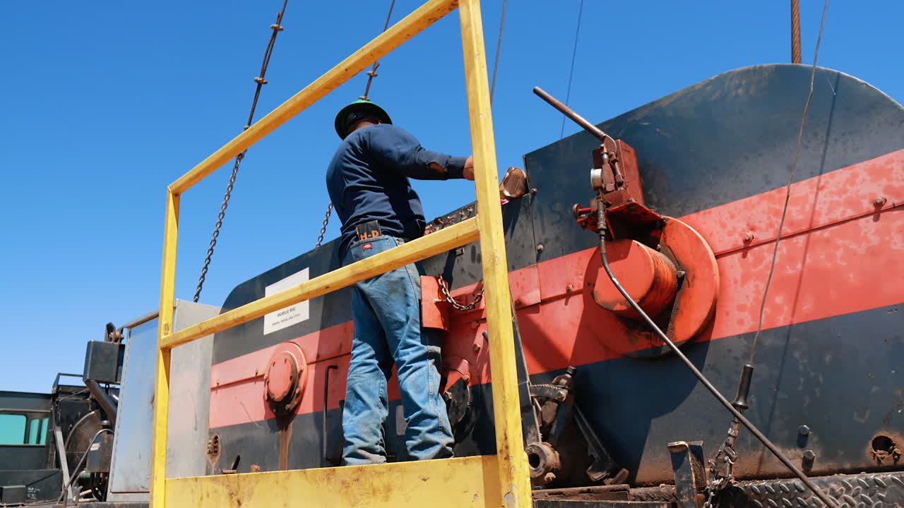 Rear view of a man standing at the deck of the machine with oil rig. Low angle view at the natural resources production worker.