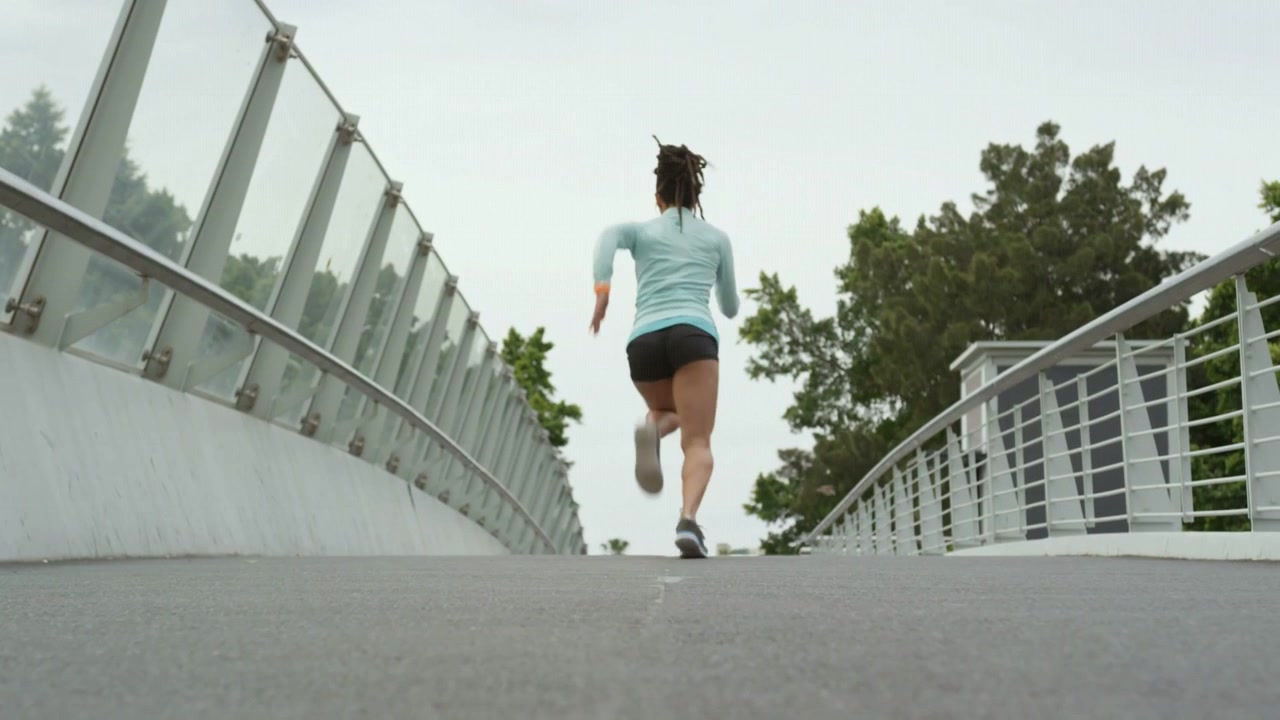 Vertical video: Starting stride near camera woman running pumping arms crossing bridge training