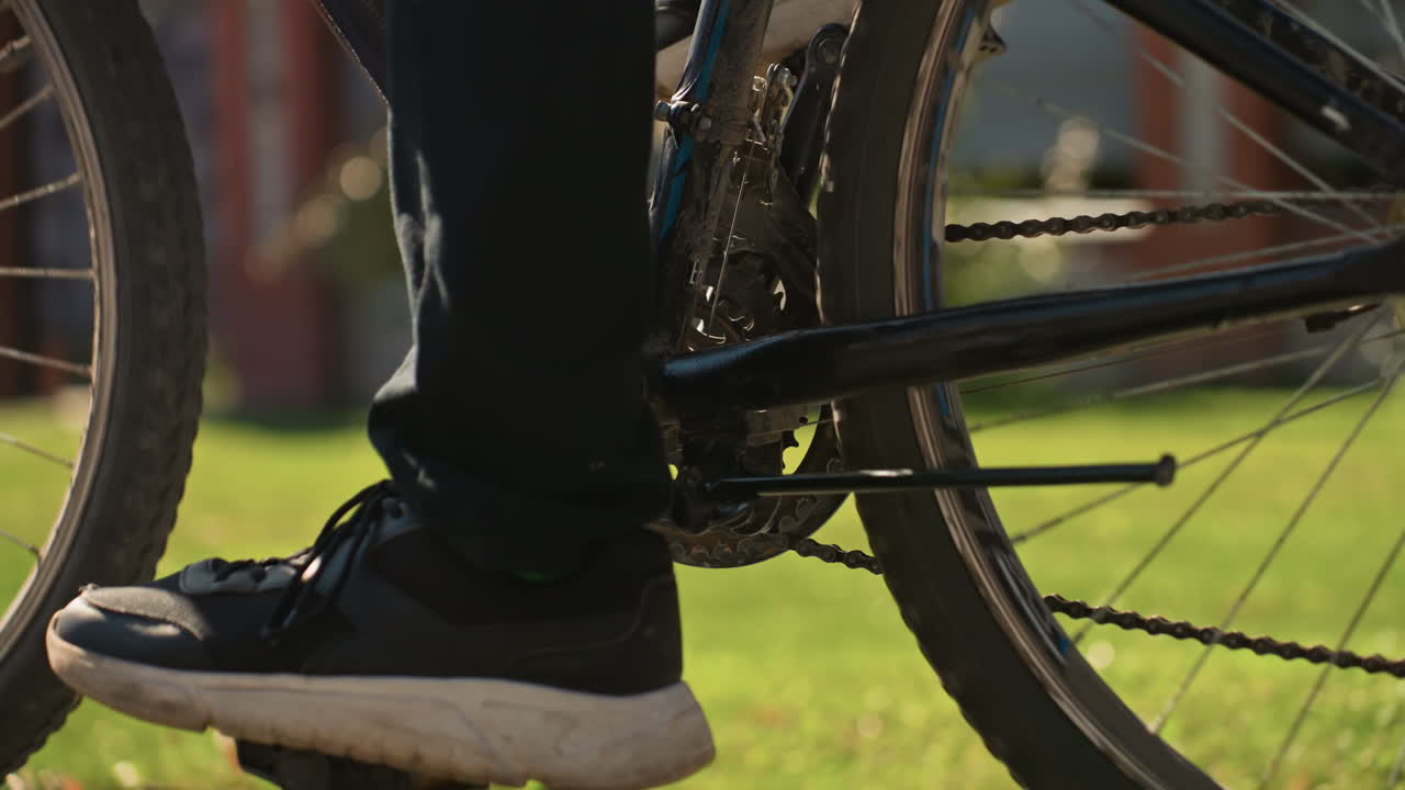 close de um pedal de bicicleta e um tênis pressionando-o, um entregador começando a pedalar em uma entrada de automóveis ensolarada, corrente e marcha em movimento, plano de fundo de um subúrbio, energia de entrega matinal, saída rápida e ritmo constante