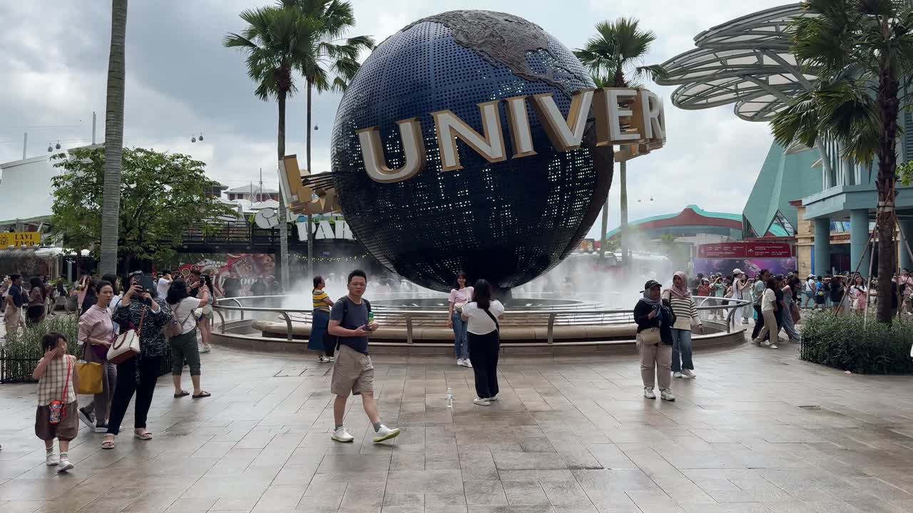 Tourists exploring and taking photos of the iconic Universal Studios Singapore Rotating Globe located within Resorts World Sentosa on Sentosa Island, Singapore.