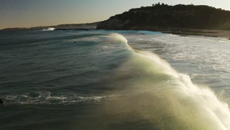 Aerial-of-beach-at-sunset,-ocean-wave-breaking-from-behind-slow-motion-in-Sydney-Australia