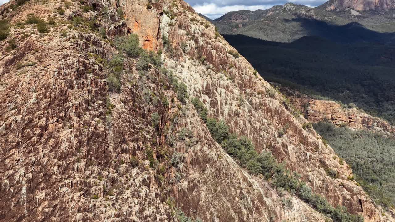 Drone camera glides above a rugged, rocky ridge surrounded by forested mountains under natural daylight, revealing dramatic terrain and expansive wilderness views