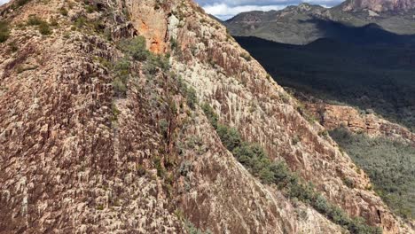 drone camera glides above a rugged, rocky ridge surrounded by forested mountains under natural daylight, revealing dramatic terrain and expansive wilderness views