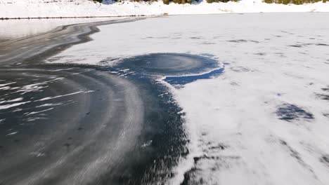 Drone-flying-along-frozen-banks-of-Palù-lake-in-Valmalenco,-Italy