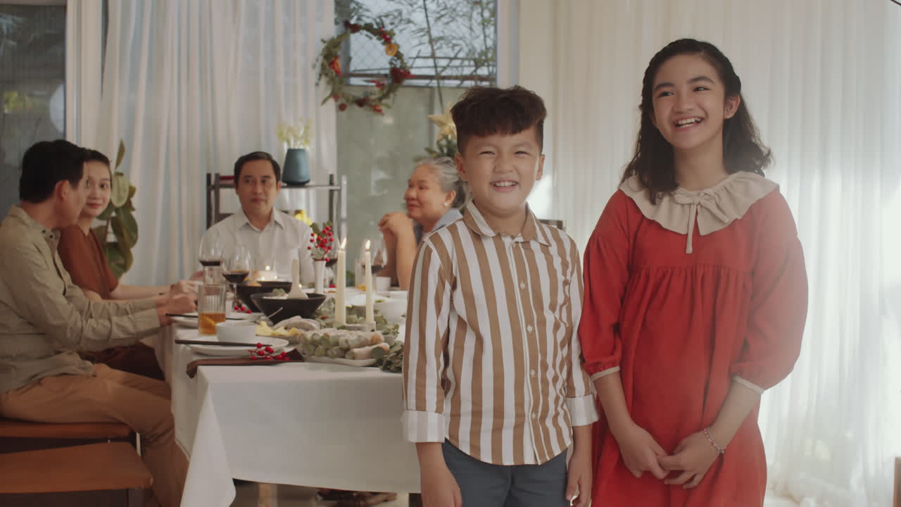 Siblings Smiling at Camera during Christmas Dinner with Family