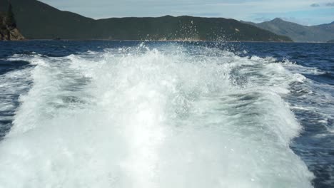 Cámara-Lenta---Parte-Trasera-De-Las-Olas-Del-Barco-Con-Cielo-Azul-Y-Montañas-En-Segundo-Plano