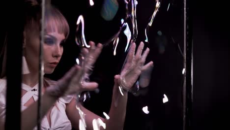 close-up: pretty girl does tricks with soap bubbles, she plays with her fingers on the wall, then blows bubble.