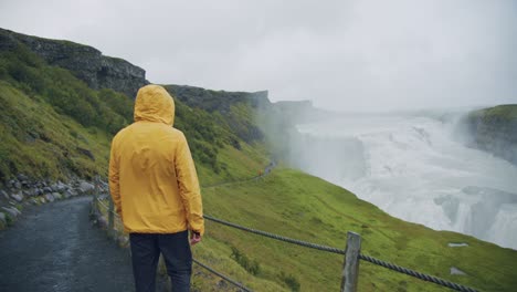 아이슬란드의 gullfoss 폭포에서 노란색 레인코트를 입은 남성 관광객.