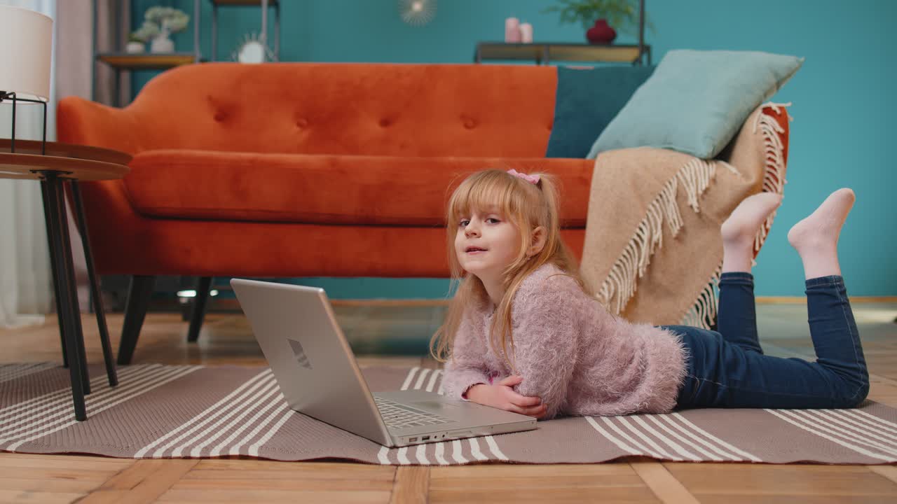 маленькая школьница использует ноутбук, учится читать, учится онлайн, учится дома одна.