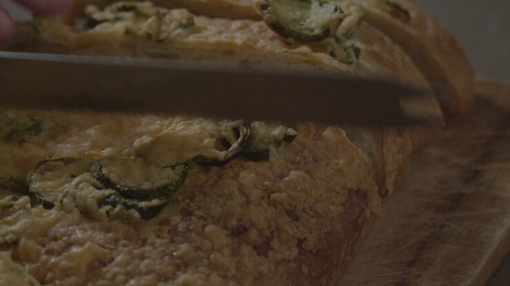 Un primo piano di pane al jalapeño che viene affettato su un tagliere di legno.