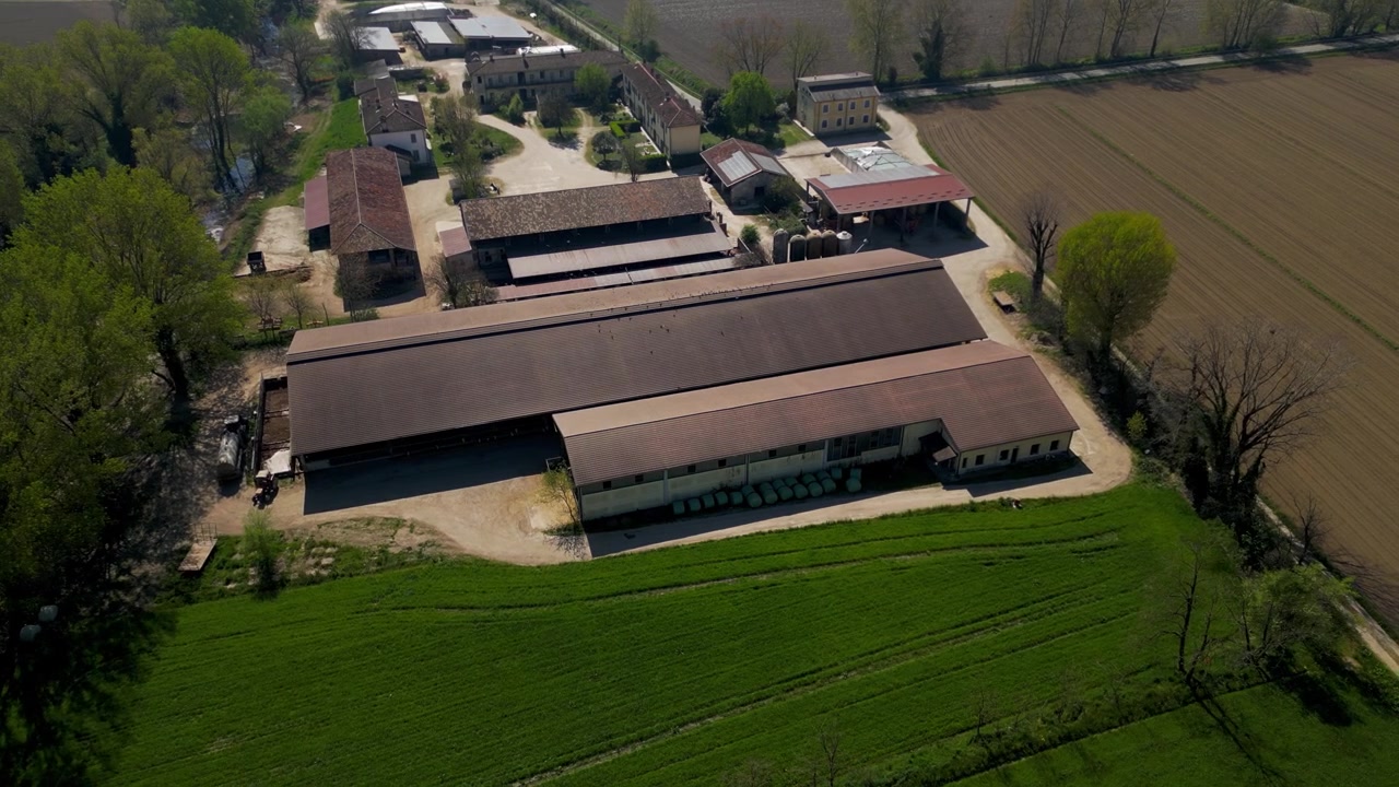 Allevamento di bestiame in Lombardia, Italia. La vista aerea evidenzia gli alloggi per il bestiame, le aree di alimentazione e i terreni agricoli che supportano la produzione agricola su larga scala.