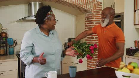 Un-Hombre-Mayor-Afroamericano-Dando-Un-Ramo-De-Flores-A-Una-Mujer-Mayor-En-La-Cocina-De-Casa