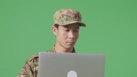 un soldado asiático usando una computadora portátil mientras camina en el estudio de fondo de la pantalla verde