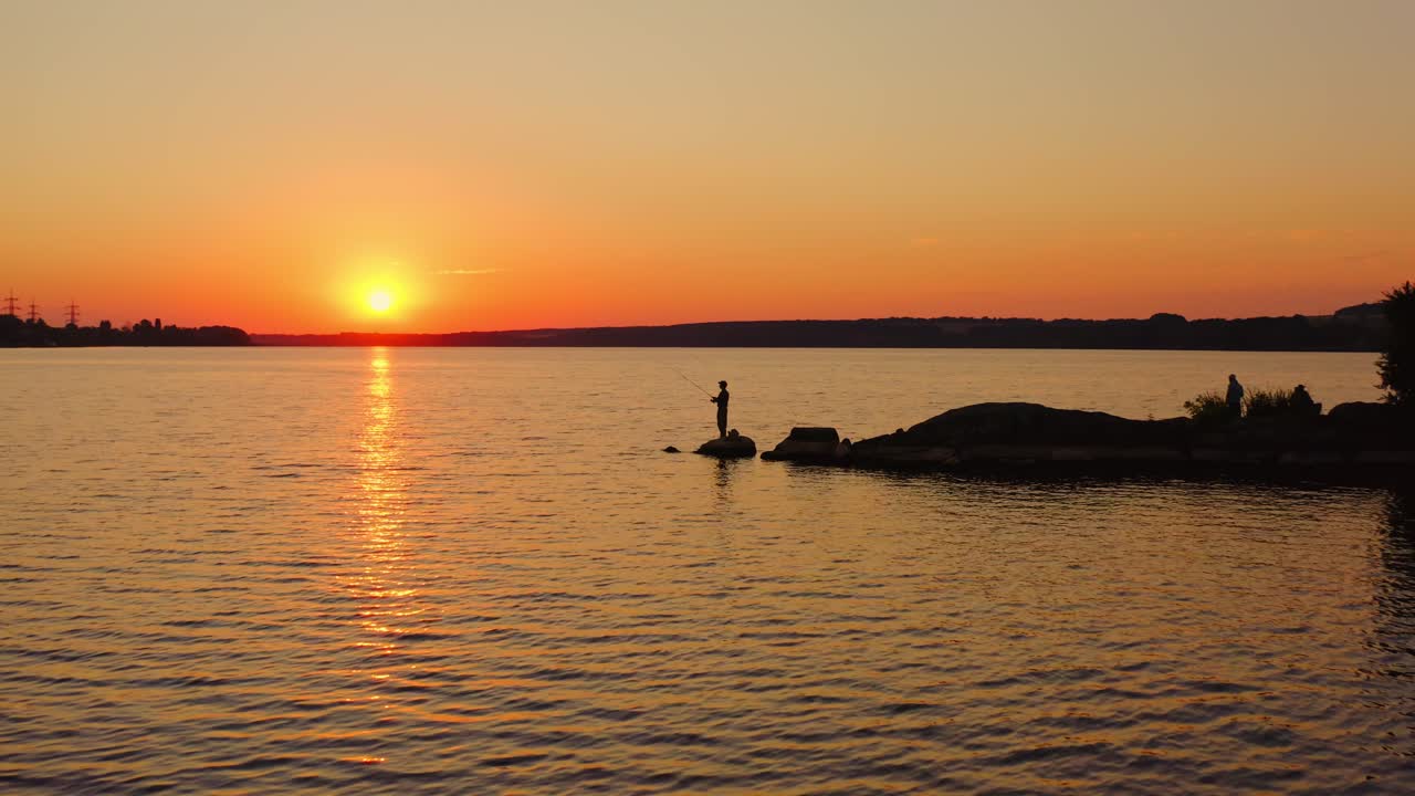The fisherman fishes at sunset. A fisherman silhouette fishing at sunset. Freshwater fishing, catch of fish. Video from a side.