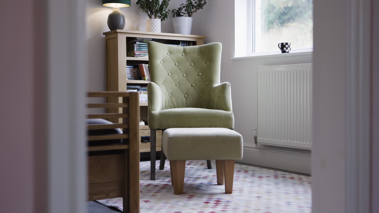 Interior of a room with an armchair, footstool, and bookshelf