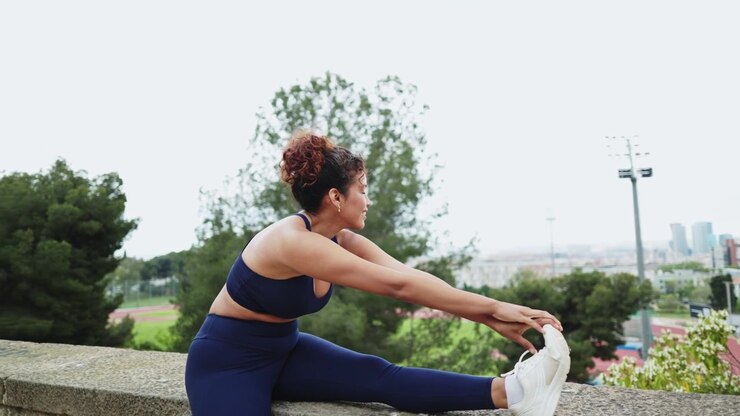 Young Woman Stretching Leg on Stone Wall in Park