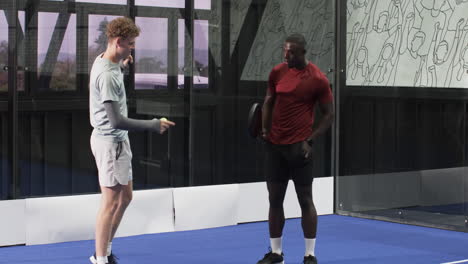 two diverse men playing padel tennis indoors, focusing on competitive game action, at indoor court
