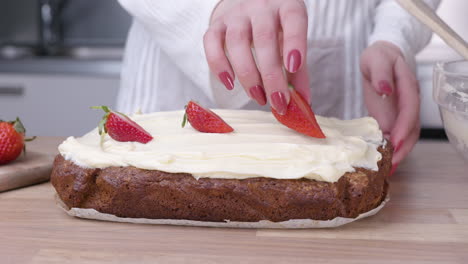 mujer poniendo fresas rebanadas de fresas en la parte superior del pastel de zanahoria horneado - de cerca