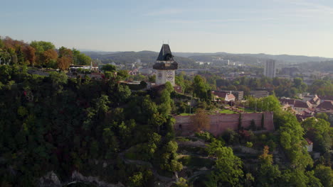 Luftaufnahme-Des-Uhrturms-Auf-Dem-Grazer-Schloßberg,-Einem-Dolomitenwald-Und-Der-Skyline-Der-Stadt-Graz