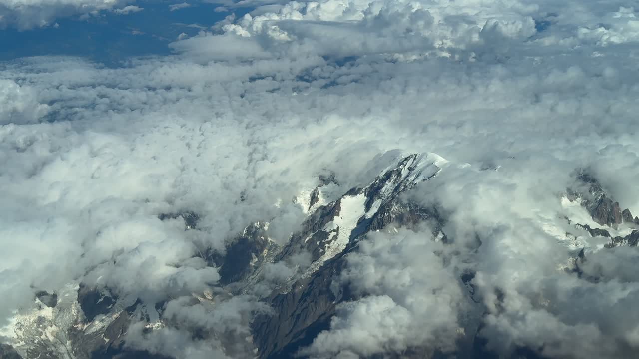 An aerial view of the Mont Blanc summit covered with few snow in a summer morning, veiled by ethereal clouds. Shot taken from a jet cokpit flying 7000m high