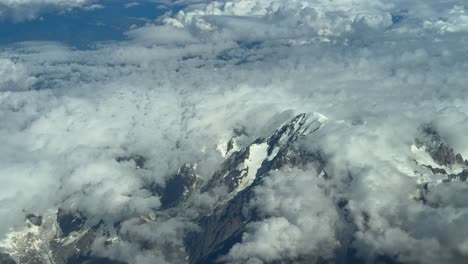 an aerial view of the mont blanc summit covered with few snow in a summer morning, veiled by ethereal clouds. shot taken from a jet cokpit flying 7000m high