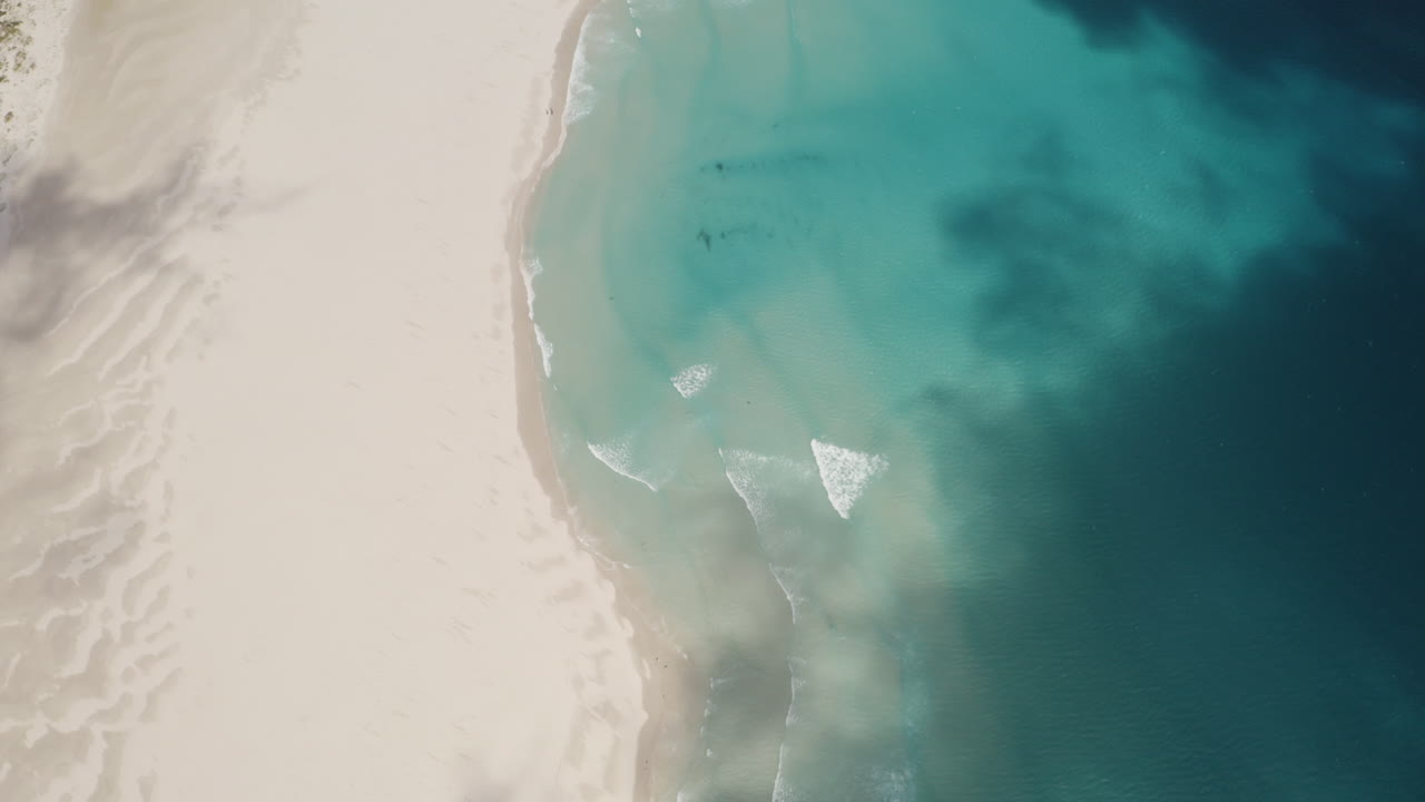 Veduta aerea dall'alto di un'ombra di nuvole cupe che passano sopra una spiaggia sabbiosa paradisiaca in Sudafrica con le onde dell'oceano sottostanti