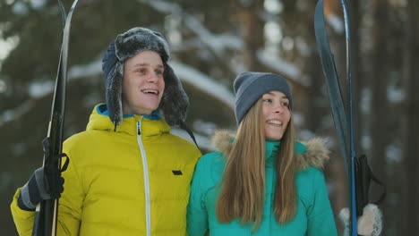 Side-view-portrait-of-active-young-couple-enjoying-skiing-in-beautiful-winter-forest,-focus-on-unrecognizable-woman-holding-ski-poles,-copy-space