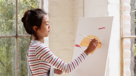 asian young woman painting on canvas at home with smiling woman, enjoying creative time