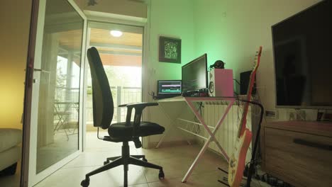 un estudio vacío de edición y grabación de video en jerusalén, con silla negra y guitarra eléctrica en la habitación, iluminado por el fuerte sol desde el balcón