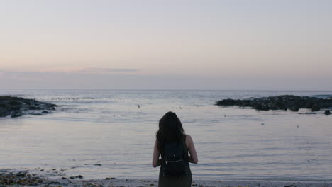 portrait of brunette woman walking on beach taking photo of seaside using phone