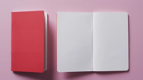 Close-up-of-open-blank-book-and-red-closed-book-with-copy-space-on-pink-background-in-slow-motion