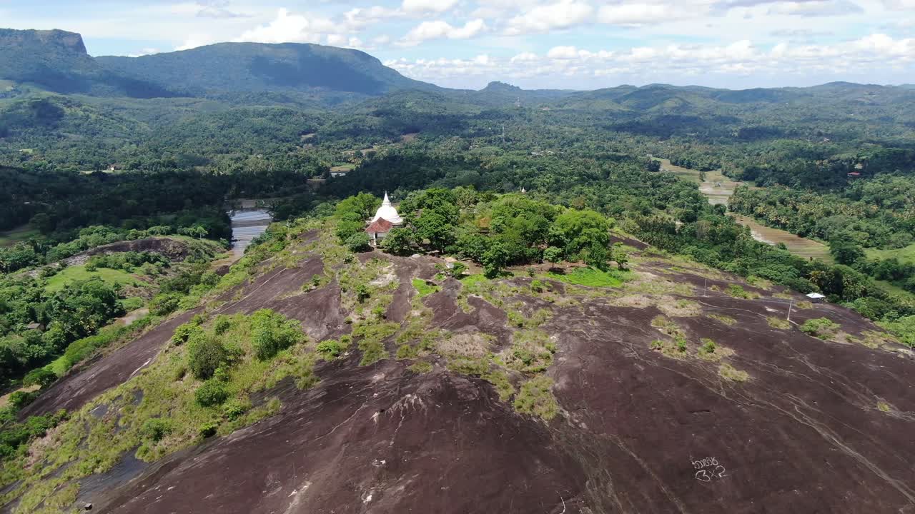 Vitt stupatempel på toppen av en kulle på Sri Lankas landsbygd, populär vandringsdestination Bible Rock i bakgrunden