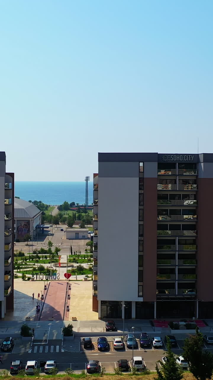Flying between the similar beautiful buildings in the cityscape of Bar, Montenegro. Lovely green area at the shore of Adriatic Sea from air. Vertical video