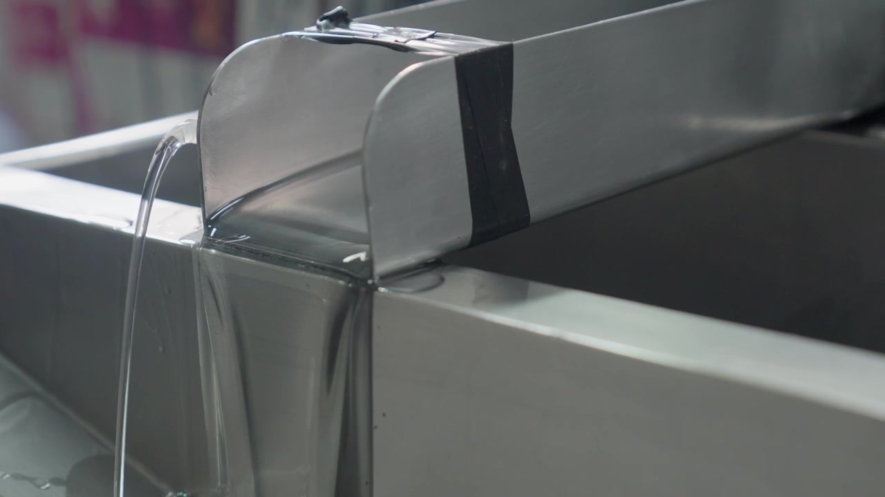 Líquido transparente sendo derramado de uma máquina industrial durante o processo de fabricação em uma planta industrial.