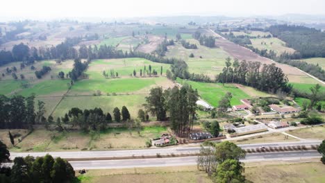 Aerial-pan-view-of-green-fields-situated-near-highways-and-local-houses