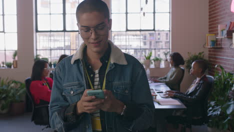 joven estudiante de raza mixta feliz usando un teléfono inteligente navegando mensajes de redes sociales enviando mensajes de texto en el teléfono móvil caminando en un lugar de trabajo de oficina diverso