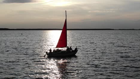 silueta de un velero con vela roja durante la puesta del sol