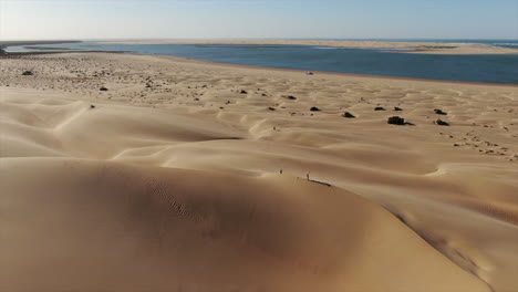 Sobrevuelo-De-Dunas-Y-Vista-Sobre-El-Horizonte-De-La-Laguna-Naila-Ubicada-En-La-Provincia-De-Tarfaya,-Sahara,-Marruecos