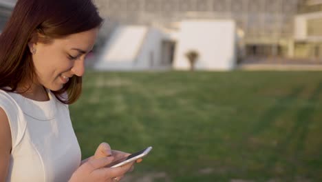 side view of smiling redhead woman typing on smartphone.